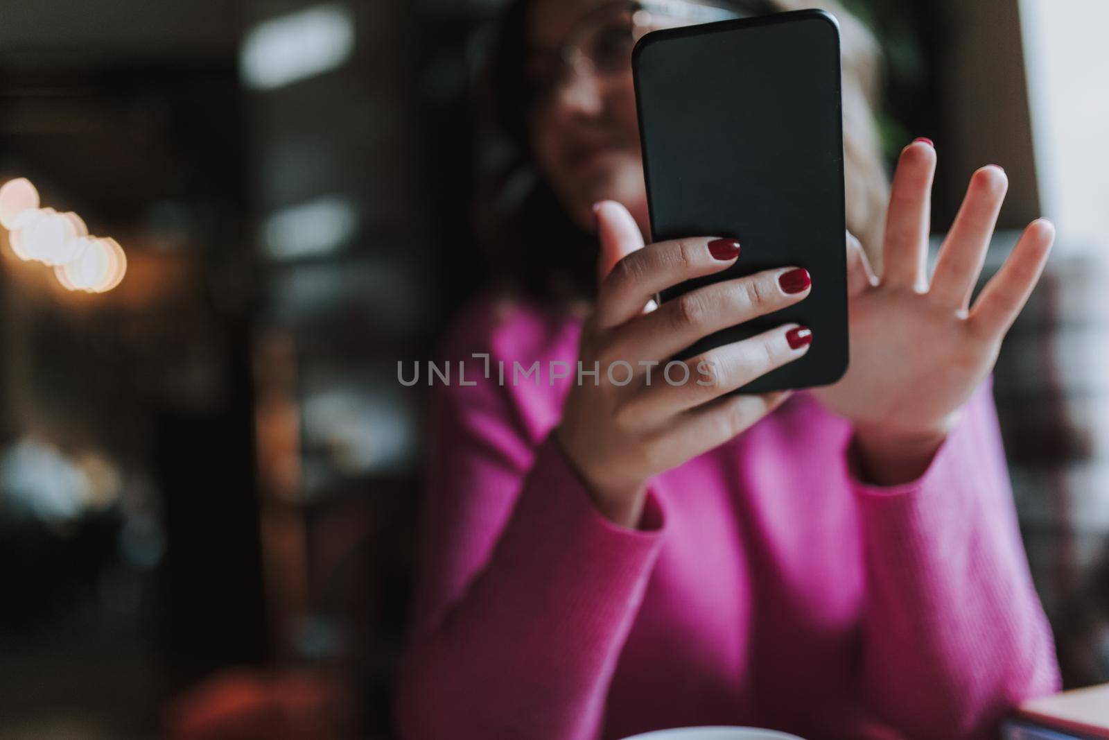 Close up of smiling beautiful woman using smartphone while typing message in coffee house