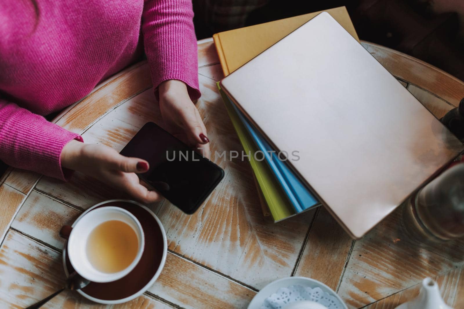 Top view of young woman sitting at the table with tea and typing on smartphone in cafe