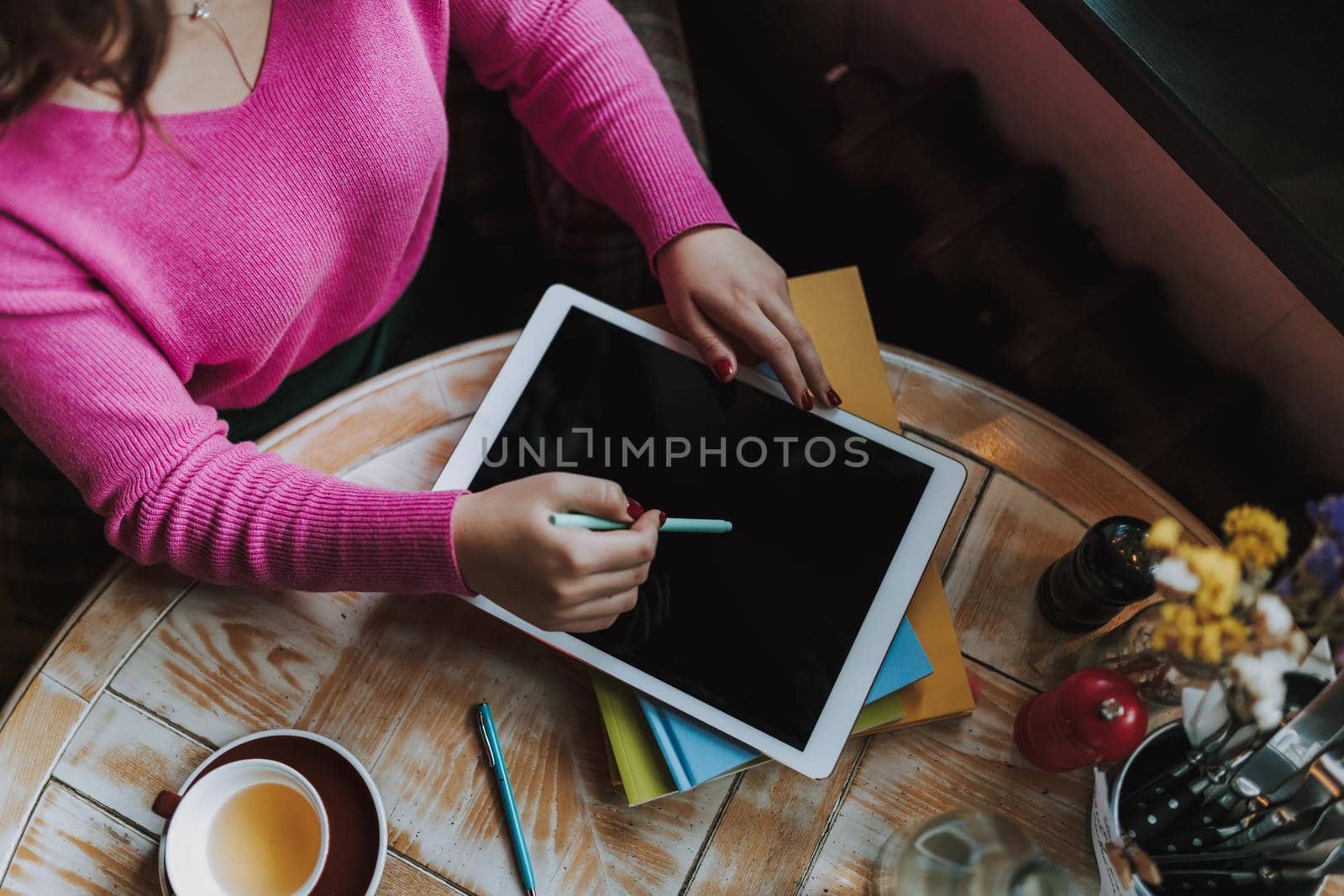 Top view of lady sitting at wooden table and working with digital tablet and drinking tea in cafe