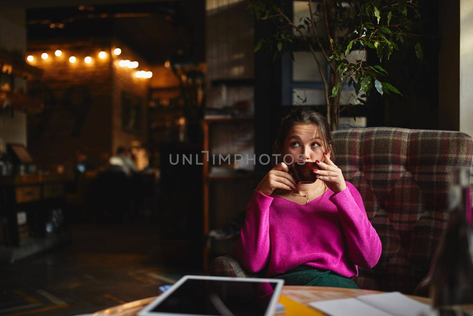 Young woman sitting in cozy armchair with hot drink by monakoartstudio