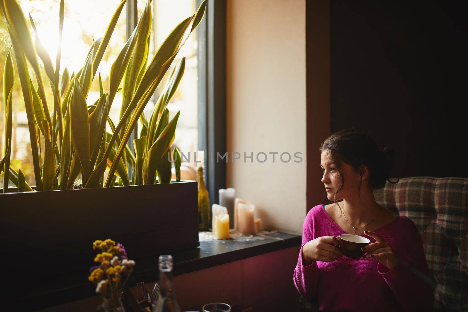 Young brunette looking out the window in cozy coffee house by monakoartstudio