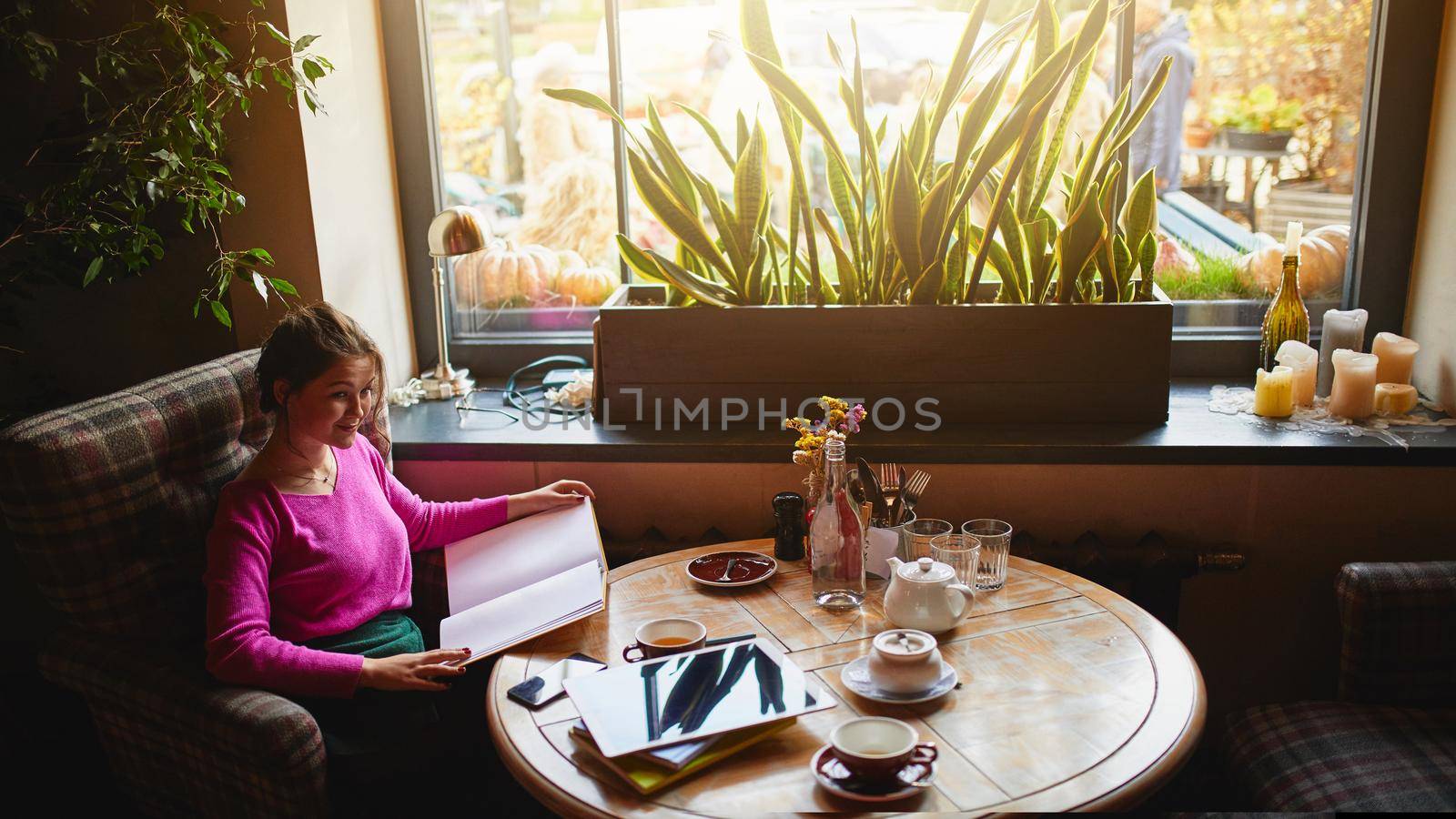 Attractive woman holding book in cozy cafe by monakoartstudio