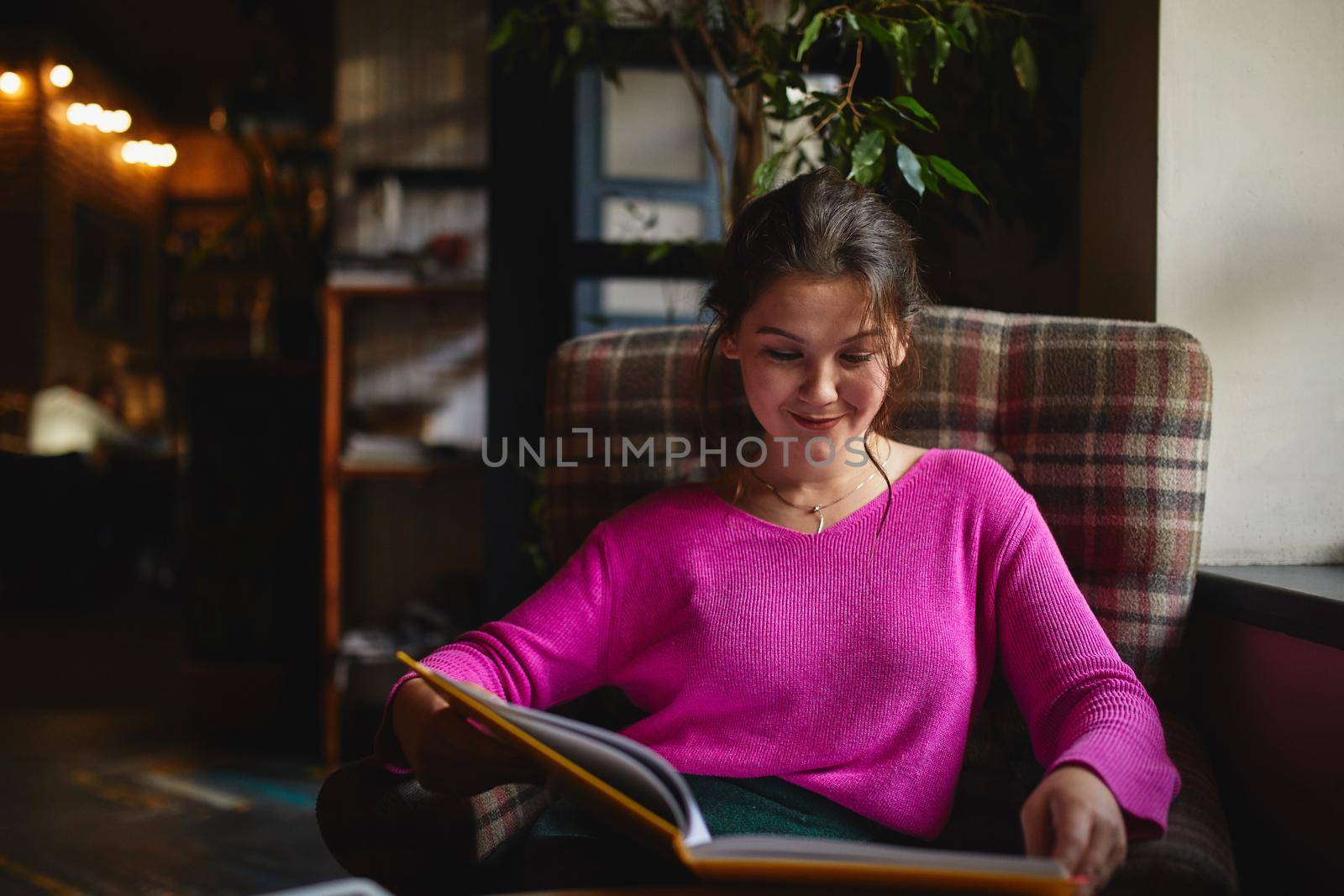 Happy young woman reading book in cafe by monakoartstudio
