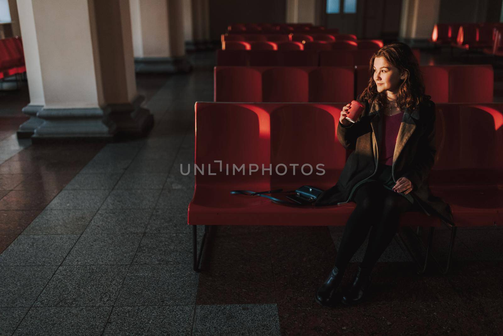 Happy pretty lady staying in waiting room on station while holding coffee