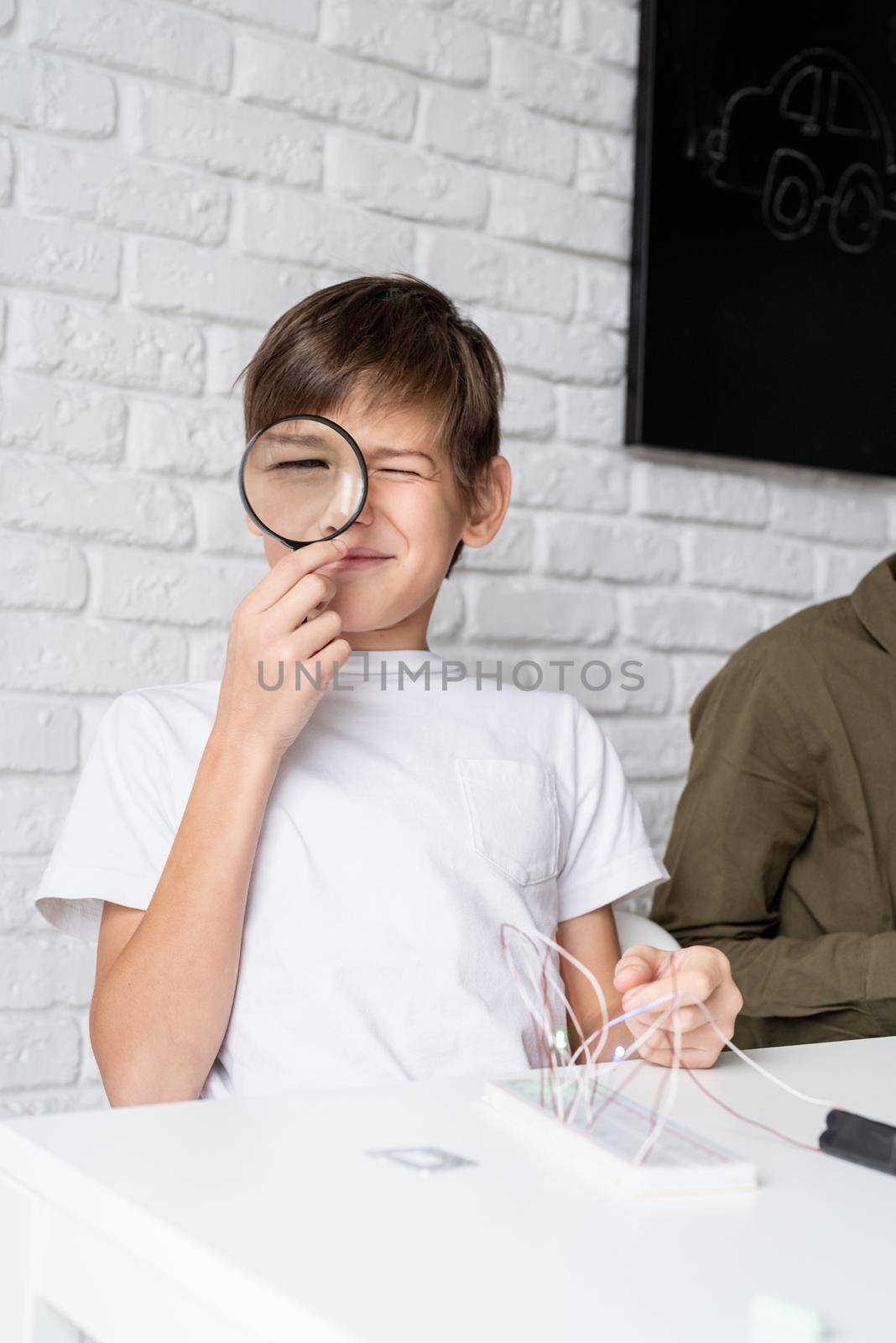 boy working with LED lights on experimental board for science project using magnifying glass by Desperada