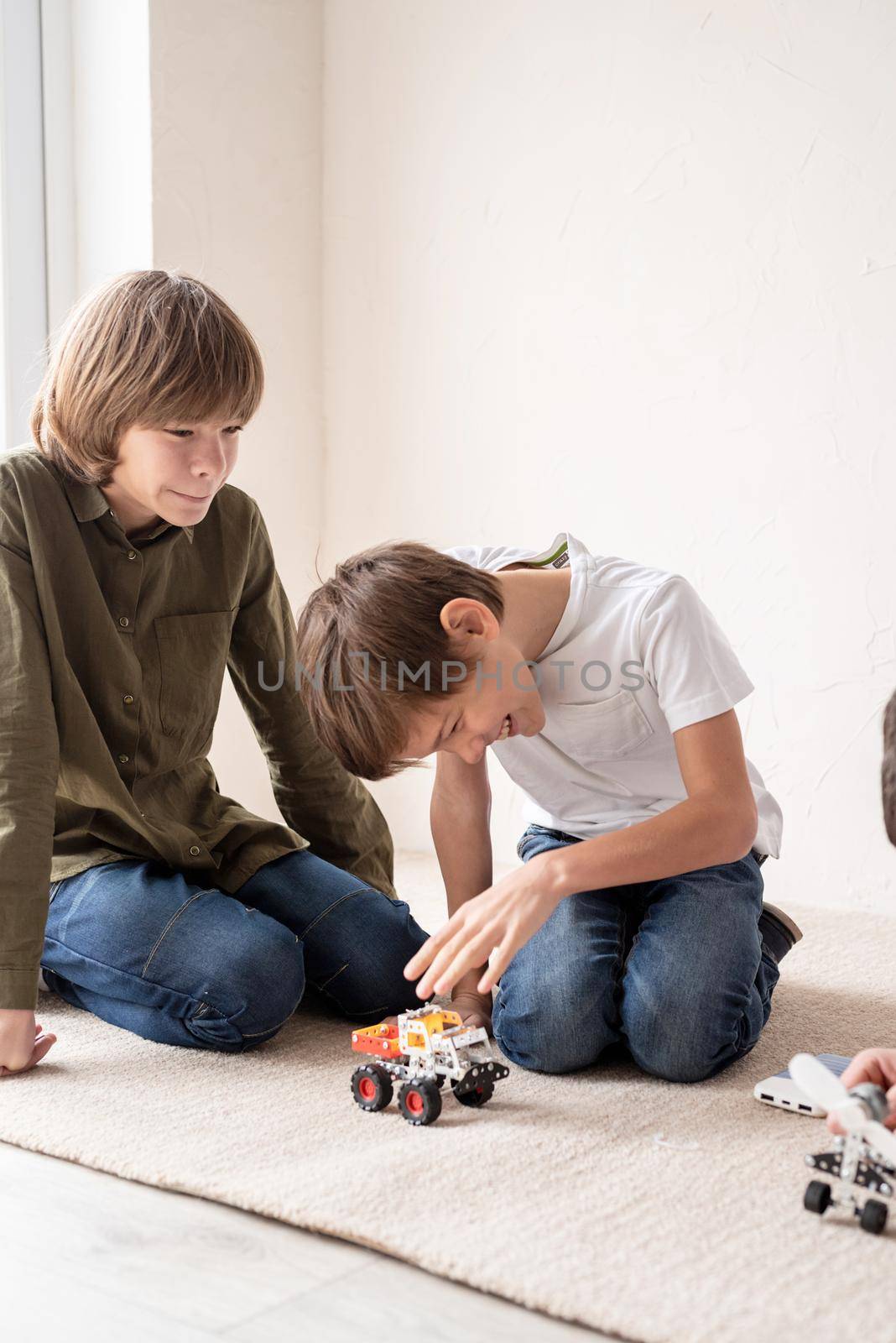 Young boys having fun constructing robot cars sitting on the rug by Desperada