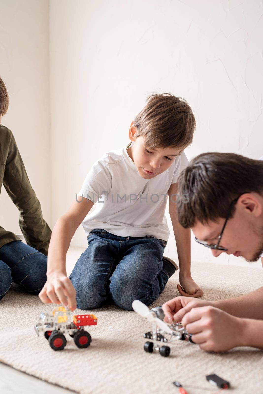 Father and his sons spending time together, having fun constructing robot cars at home sitting on the rug