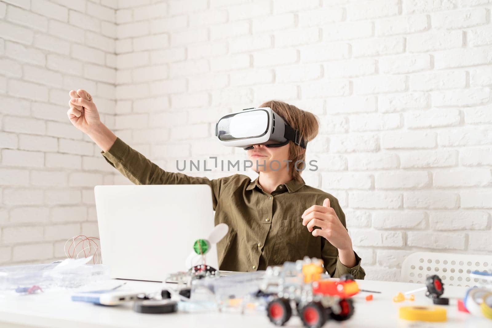 Nice teen boy in VR glasses sitting at the table playing game