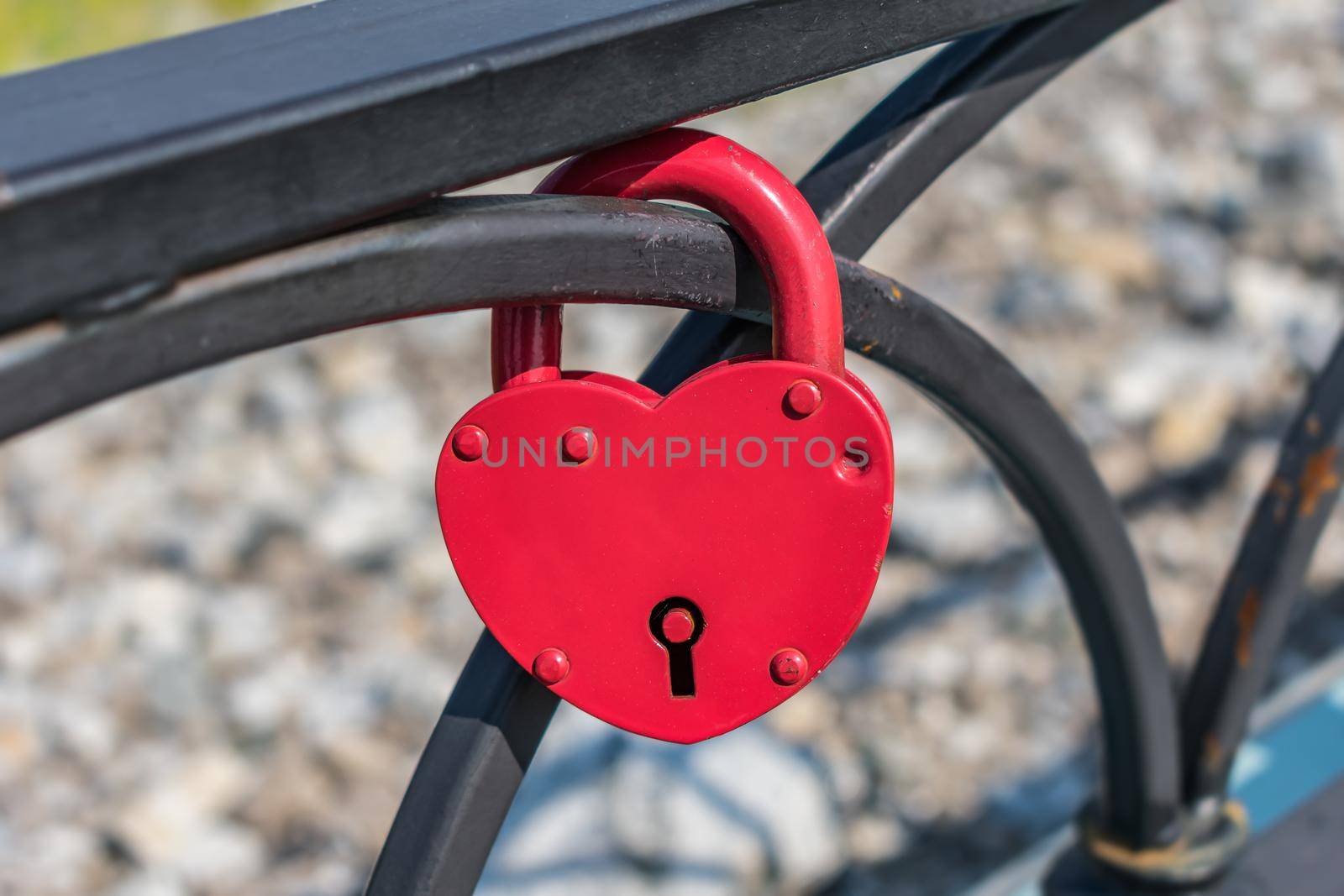 Red heart-shaped pendant lock hanging from the fence as a symbol of marriage