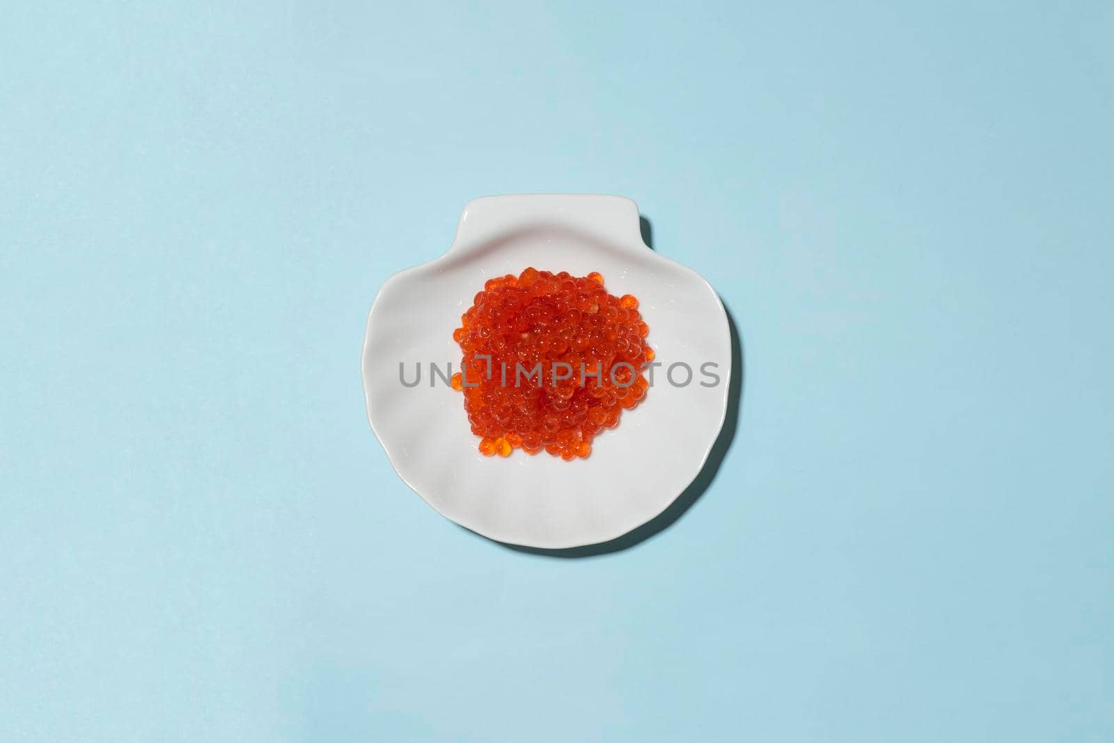 Porcelain plate with red caviar on a blue background.