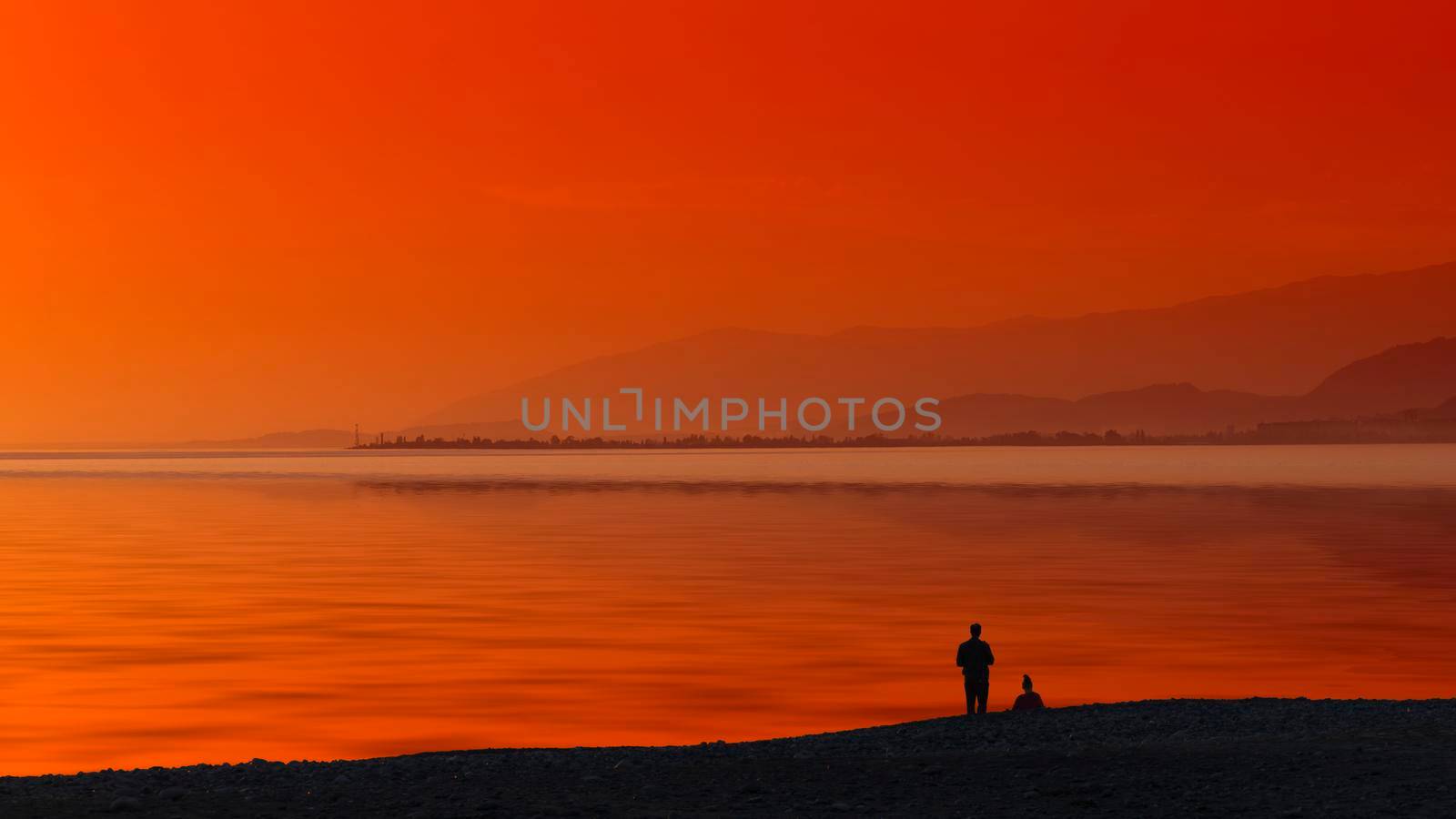 Seascape with orange sunset and silhouettes of people on the beach.