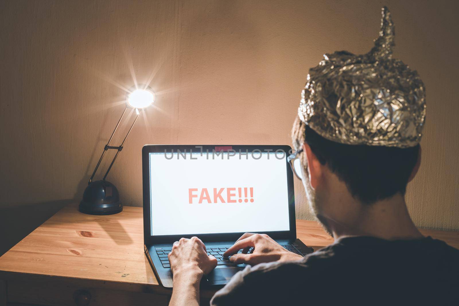 Young man with aluminum cap is sitting in the dark basement in front of a laptop. Conspiracy theory concept