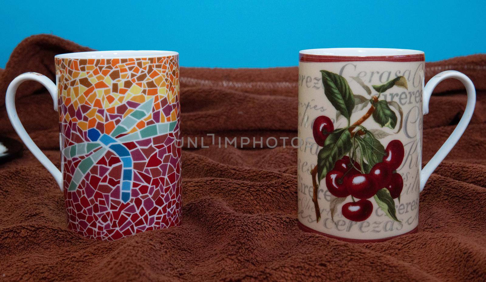 Two tea cups with beautiful prints on brown tablecloth and blue background