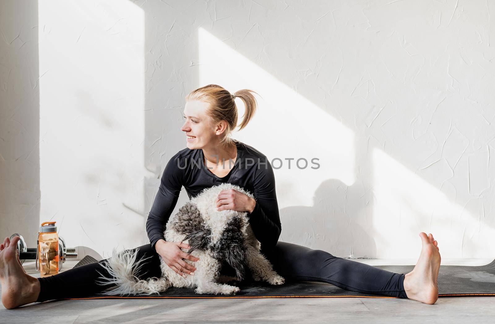 Healthy lifestyle. Sport and fitness. Happy young blond woman patting her dog at the home gym