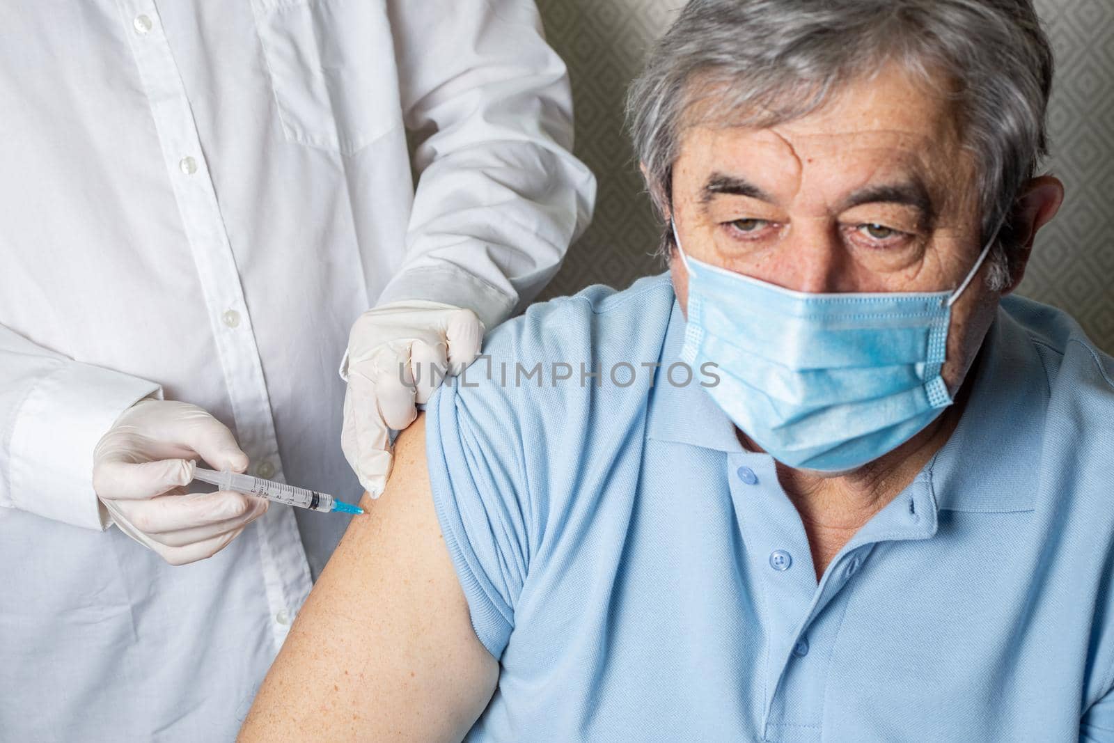 Senior elderly man being vaccinated against coronavirus by a male doctor. General practitioner vaccinating an elderly patient against flu, influenza, pneumonia or coronavirus.