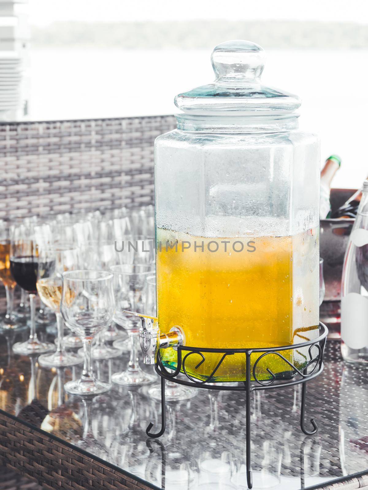 Glass decanter of cold lemonade. Transparent container with tap for soft drinks. Catering services for parties and celebrations. Outdoor bar.