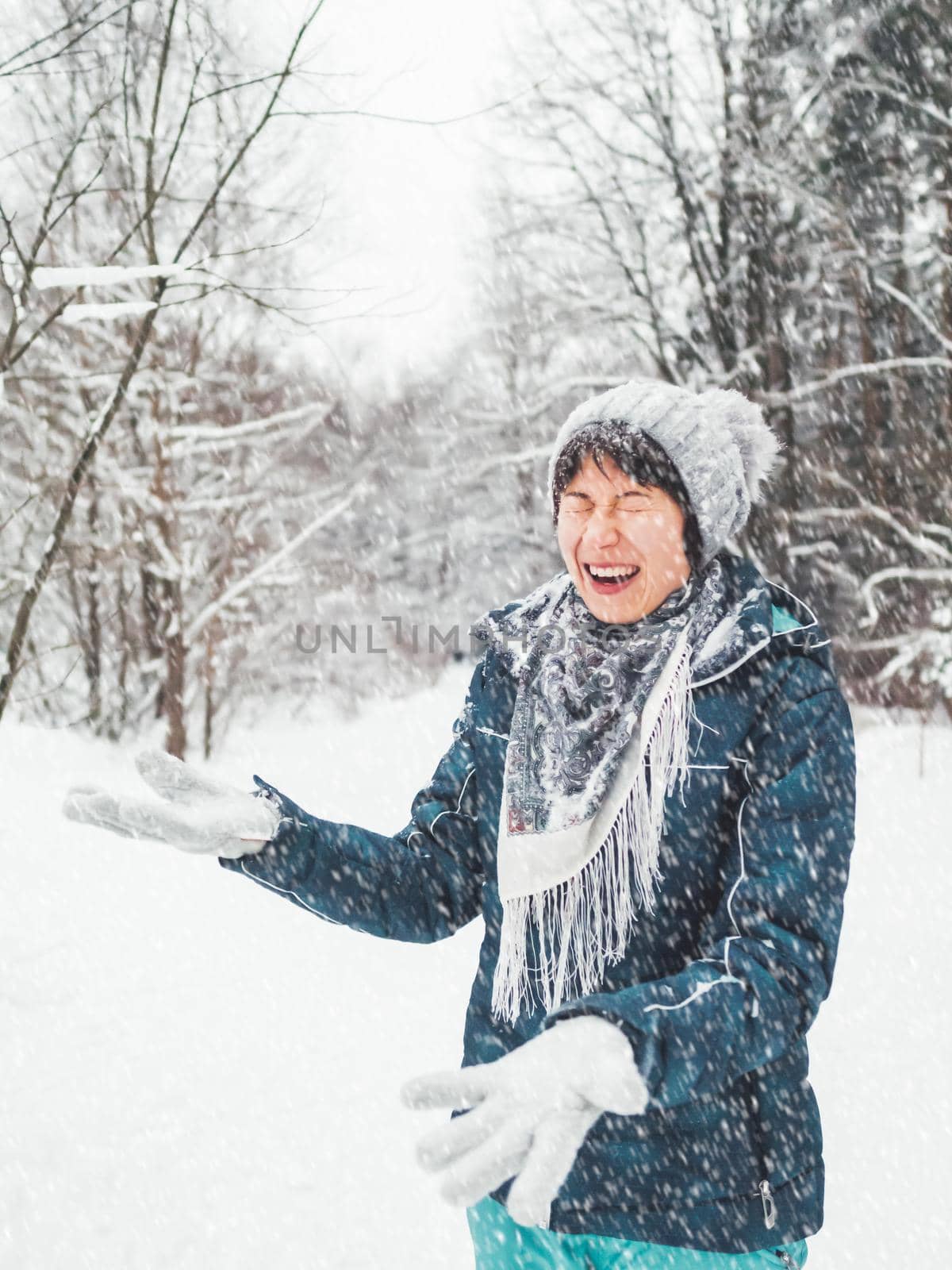 Smiling woman is playing with snow. Fun in snowy winter forest. Woman laughs as she walks through wood. Sincere emotions.