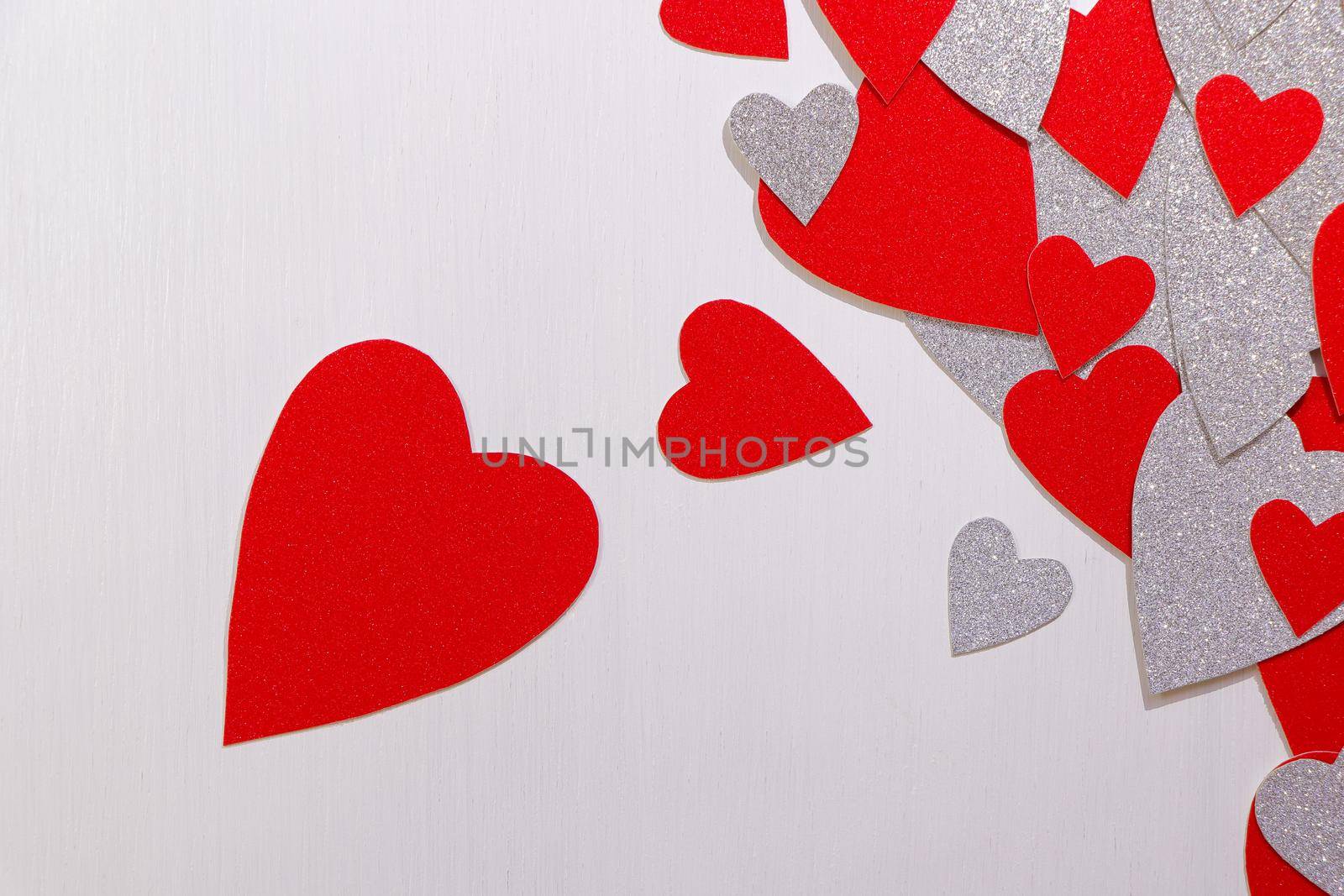 Saint Valentine's day love themed flat-lay design with heap of red and silver heart shapes on textured white