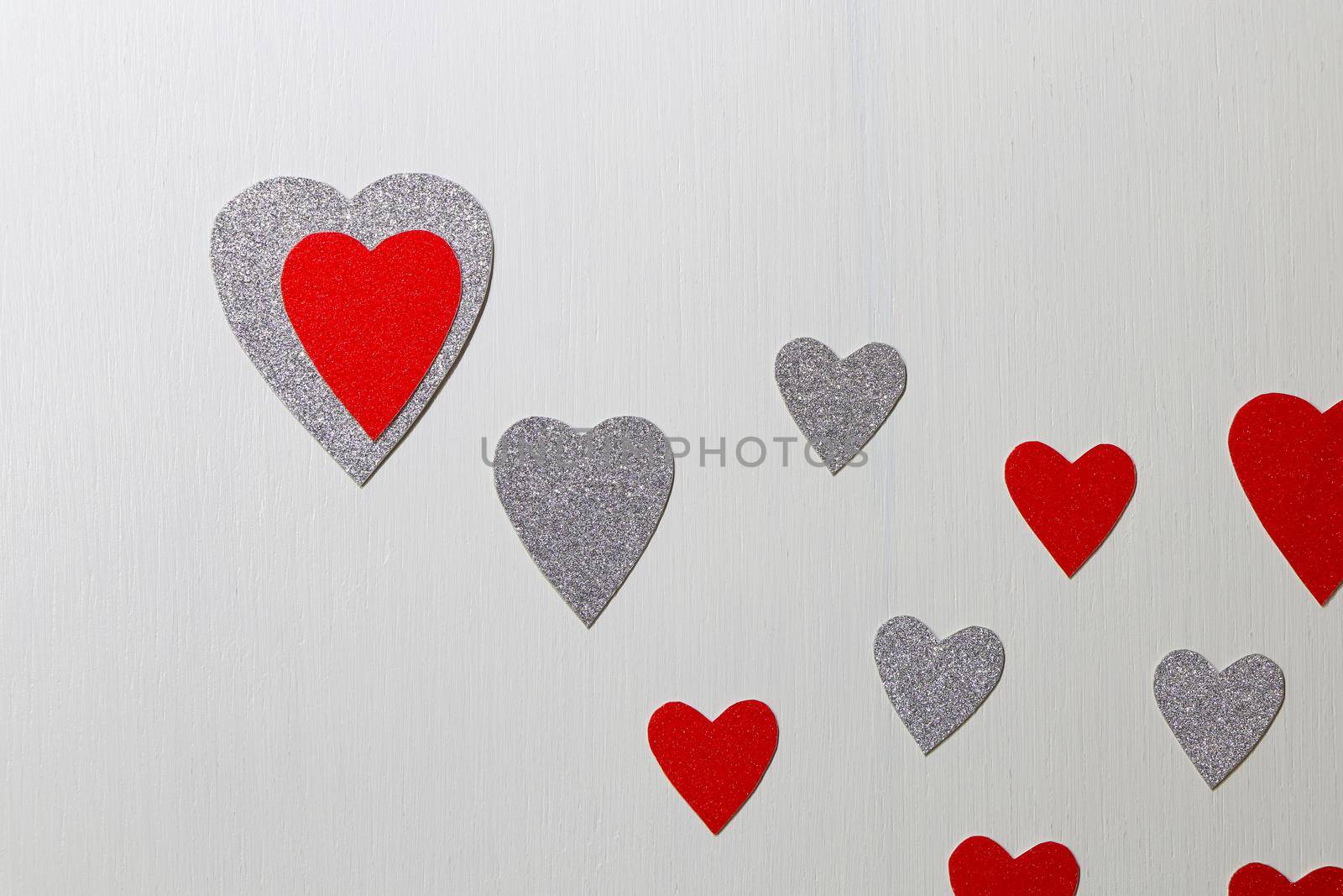 Saint Valentine's day love themed flat-lay design with red and silver hearts with trailing hearts on textured white