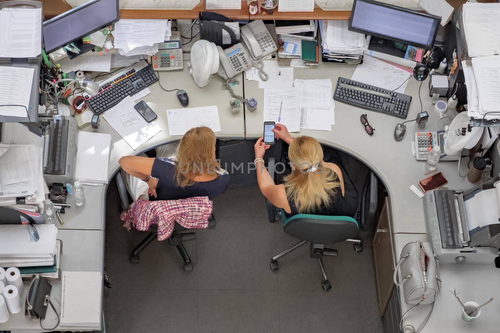 Working days of office manager worker and female showing in phone to employee or workplace communication. Two woman colleagues using smartphone in the office demonstrate message on cell phone top view