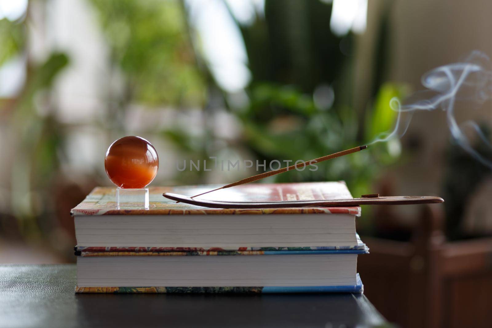 Selective focus, burning incense stick with brown glass ball on stack of books with blurred background. Concept of relaxation and meditation at home. High quality photo