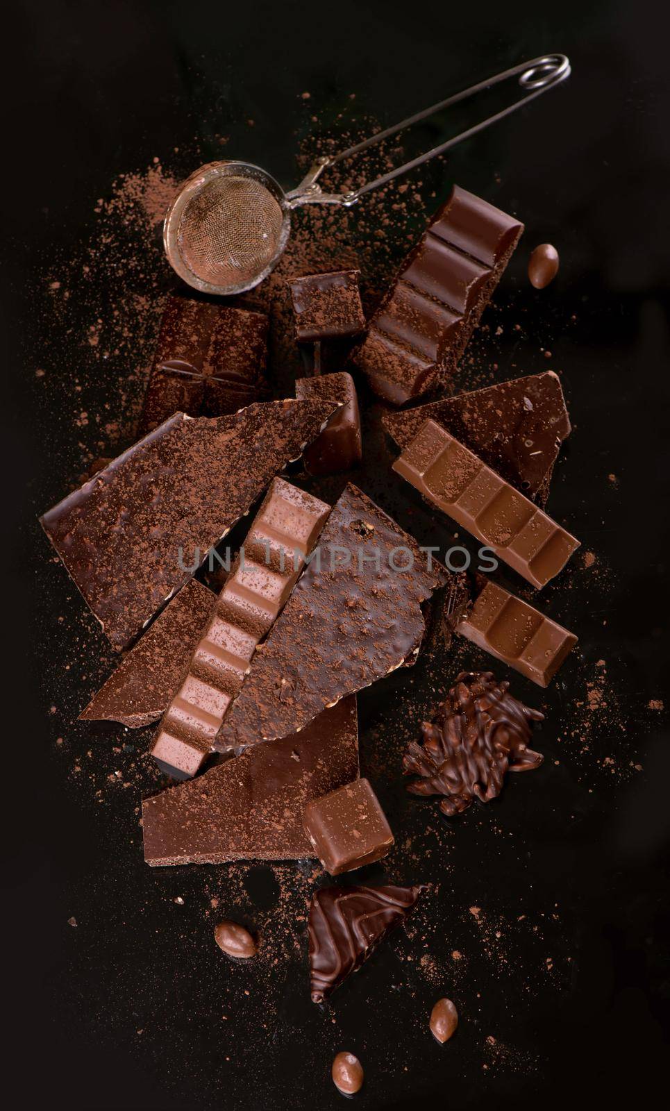 Broken chocolate pieces and cocoa powder on wooden background