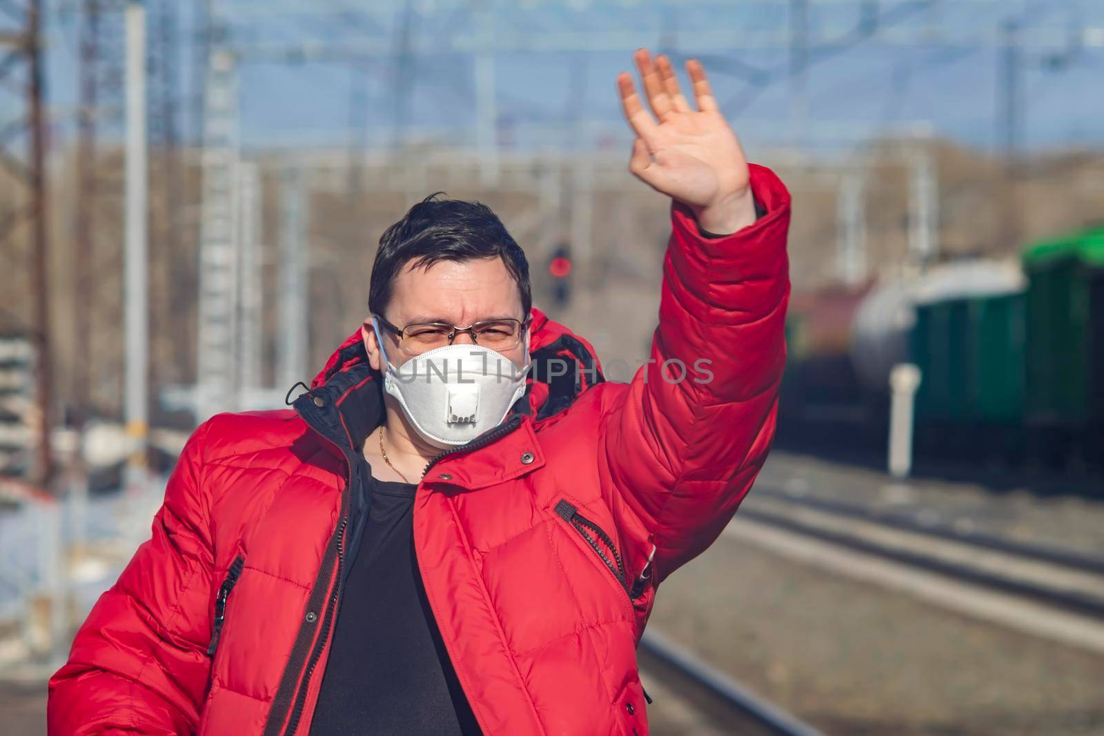 a man in a medical mask waves on the platform of a railway station by jk3030