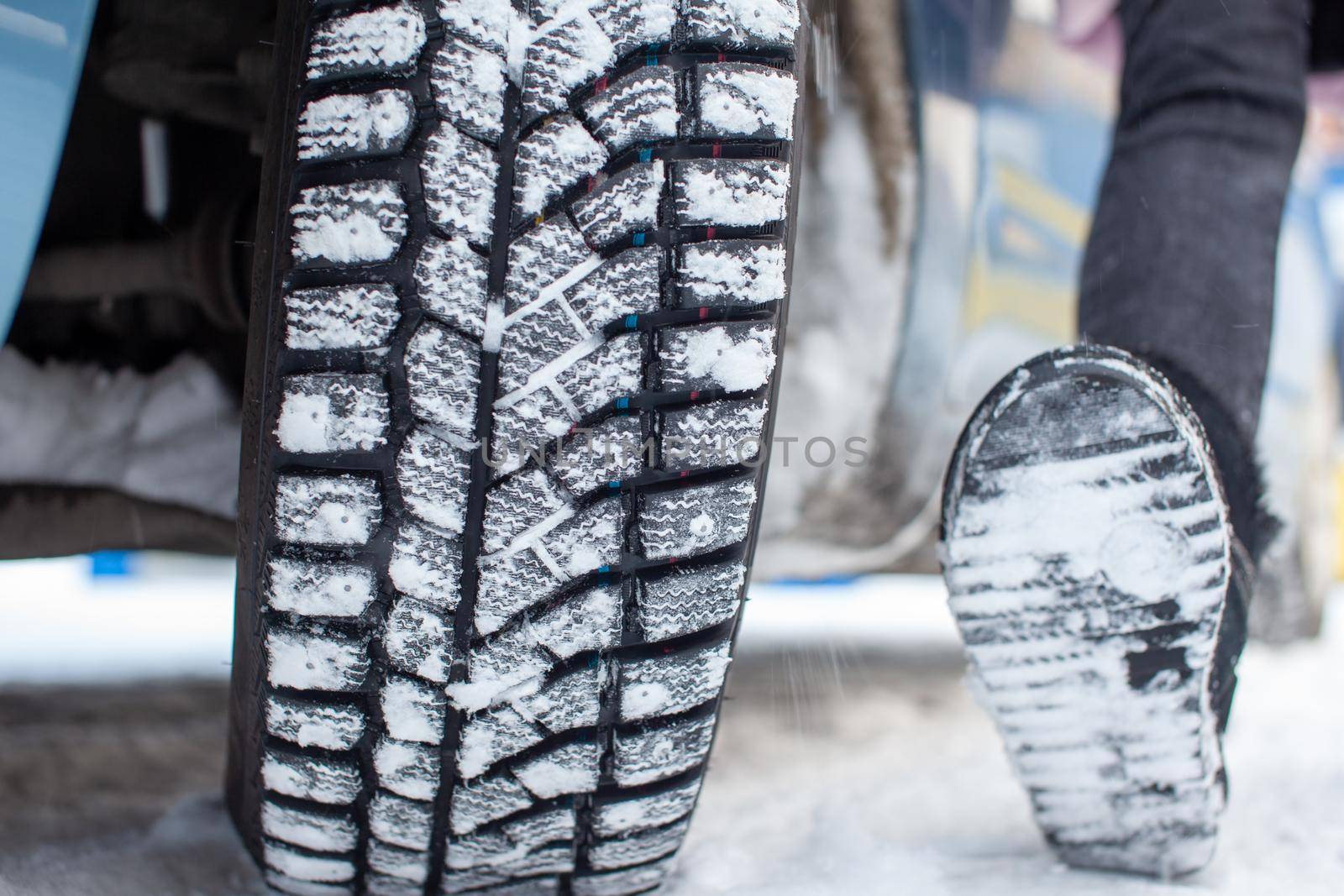 Car tires on a winter road are covered with snow. A car on a snow-covered alley. A car wheel compared to the sole of a person's shoe.