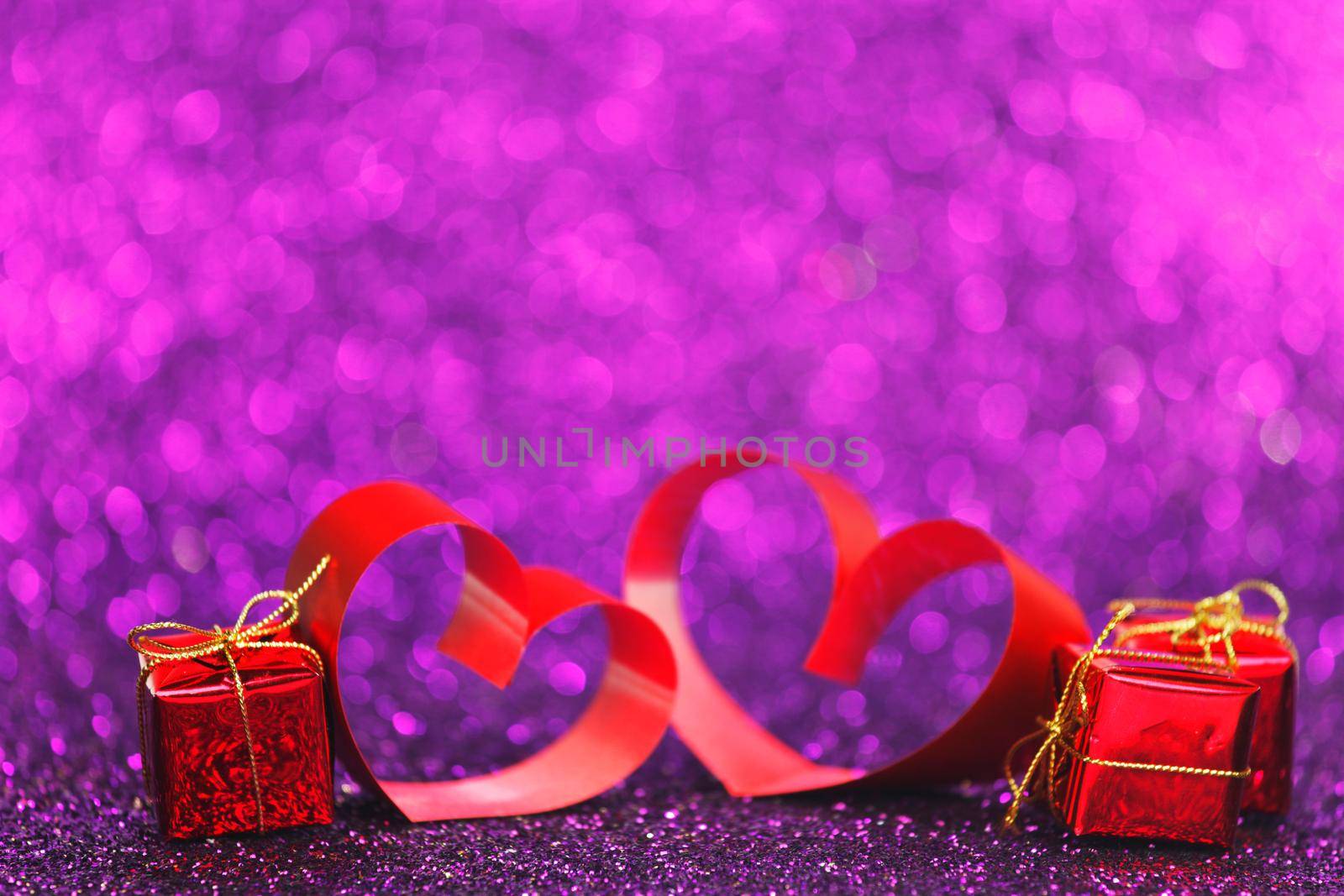 Decorative hearts of red ribbon and gifts on shiny purple glitter background