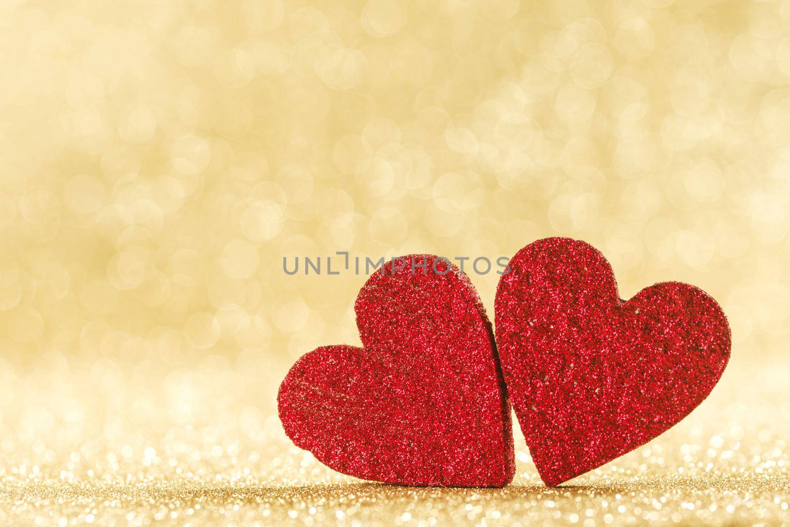 Two red hearts symbol of love on golden background with beautiful bokeh, Saint Valentine Day celebration, copy space for text
