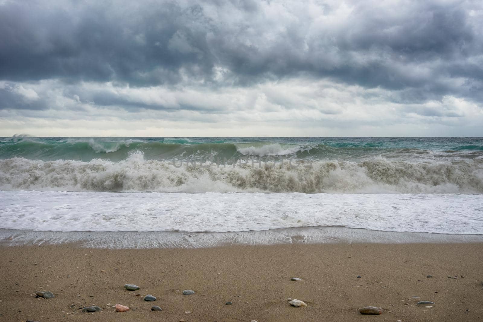 The landscape of the stormy sea under the dark clouds and the sandy beach