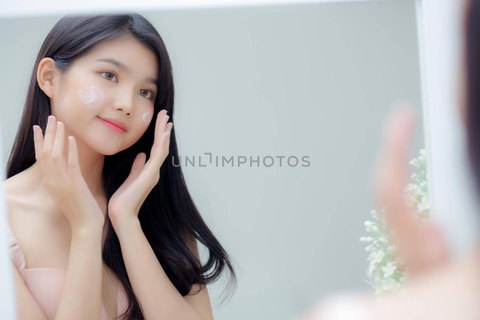 Beautiful young asian woman smiling look at mirror of checking face with skin care and cosmetic for rejuvenation and hygiene, beauty girl happy clean facial with cream or lotion and for health.