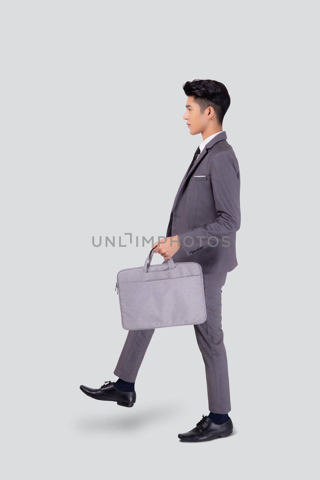 Young asian business man in suit walking movement holding bag isolated on white background, portrait of executive or manager, happy businessman holding briefcase, male with confident for success. by nnudoo
