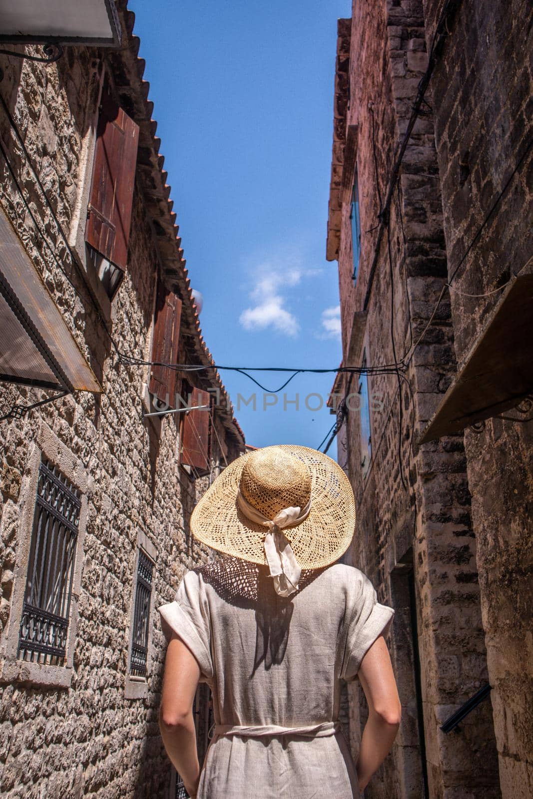 Rear view of beautiful blonde young female traveler wearing straw sun hat sightseeing and enjoying summer vacation in an old traditional costal town at Adriatic cost, Croatia by kasto