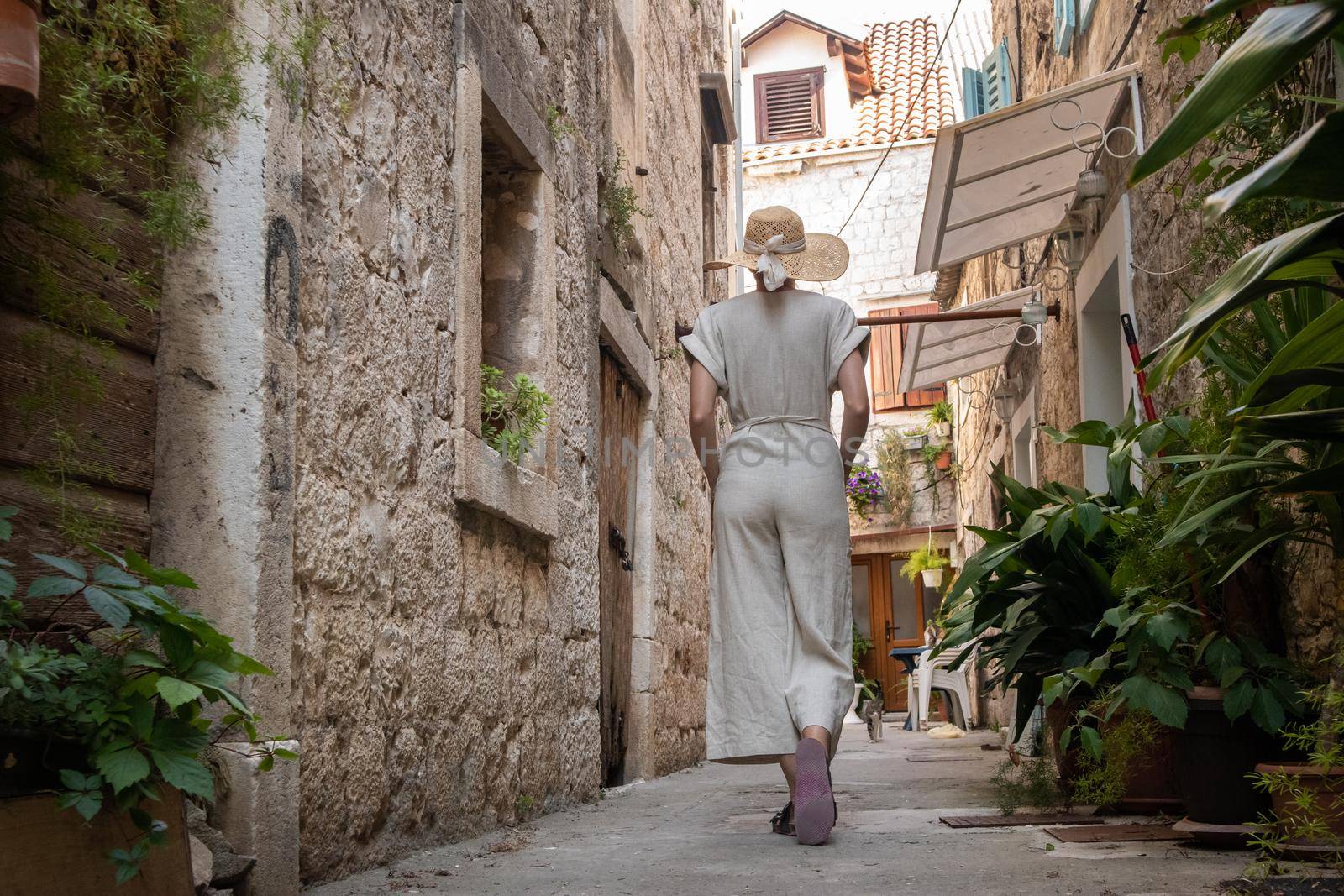 Rear view of beautiful blonde young female traveler wearing straw sun hat sightseeing and enjoying summer vacation in an old traditional costal town at Adriatic cost, Croatia by kasto