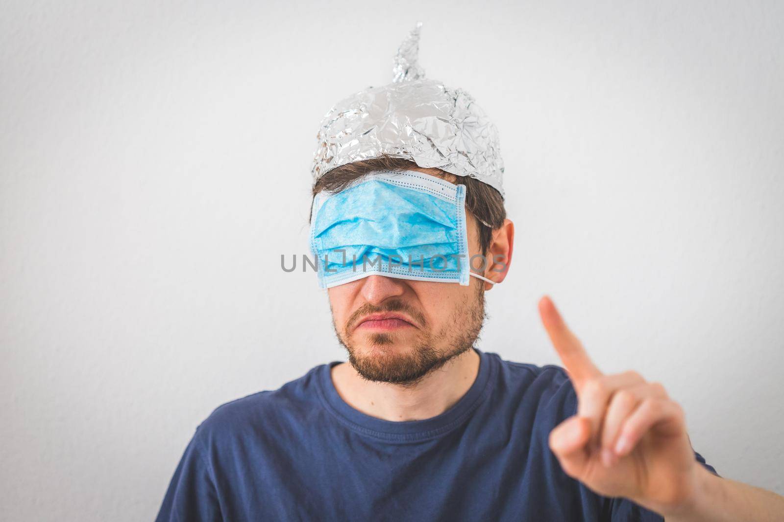 Young angry man with aluminum cap and face mask is gesturing angry. Conspiracy theory concept.