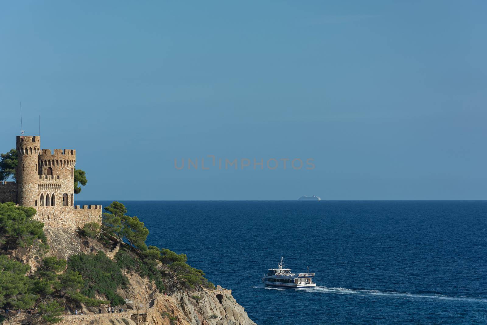 Lloret De Mar, Spain - 09/28/2019: Seascape. An old castle and a ship sailing away by Grommik