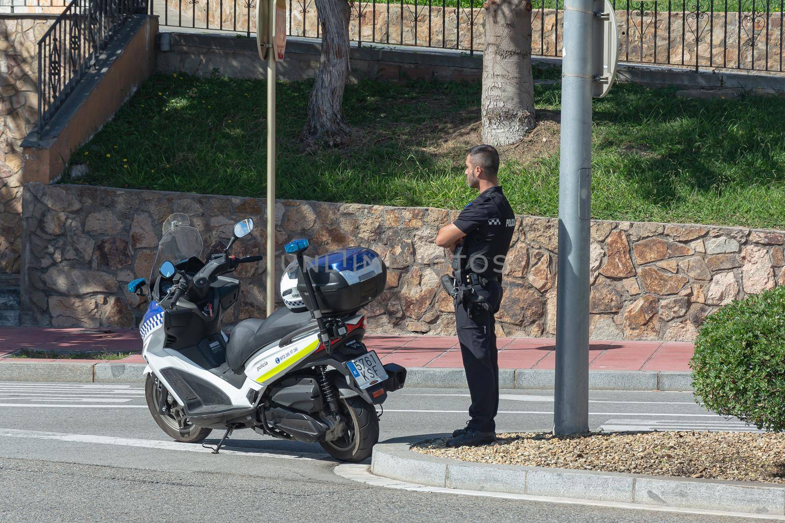 Lloret De Mar, Spain - 10/04/2019: police officer with a motorcycle at the intersection of a city street by Grommik