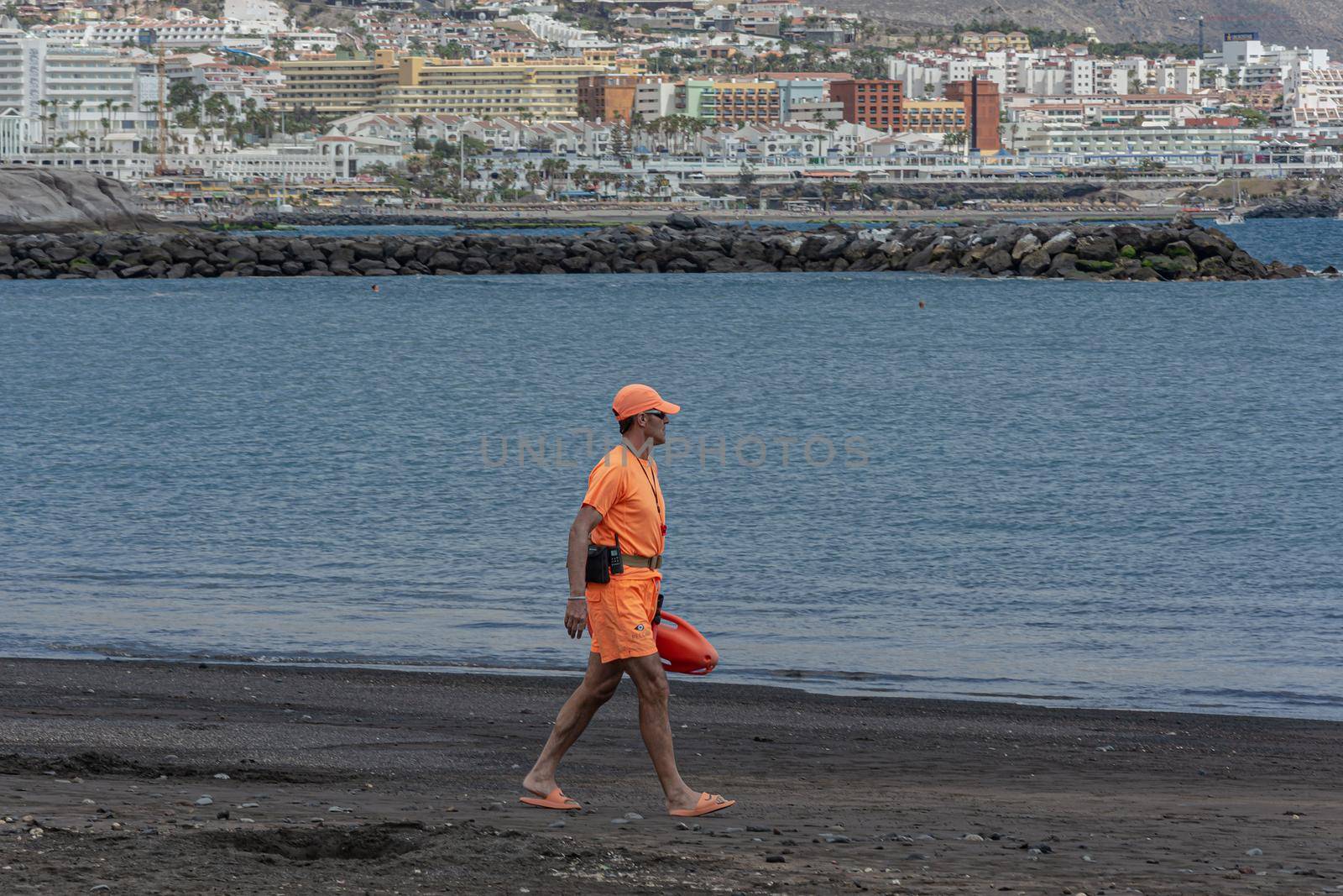 Tenerife, Spain - 05/10/2018: rescuers in an orange suit walking along the ocean, blurred background by Grommik