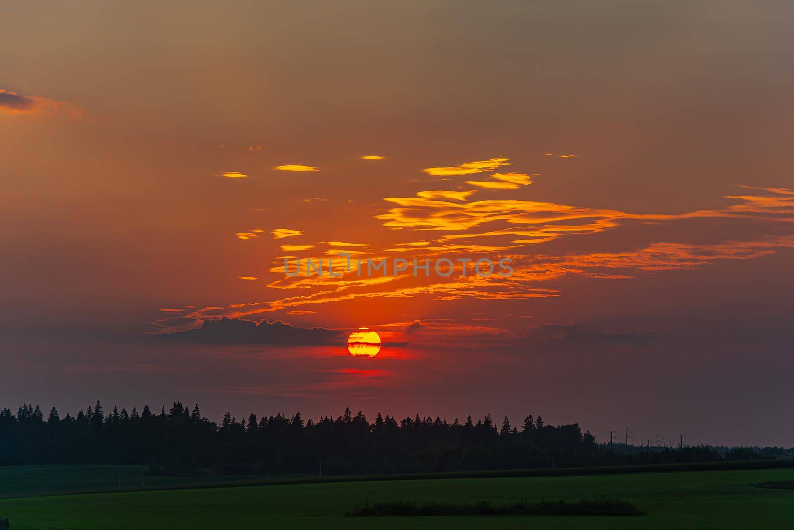 Sunset. The sun sets behind clouds against a background of green forest and fields. Stock photography