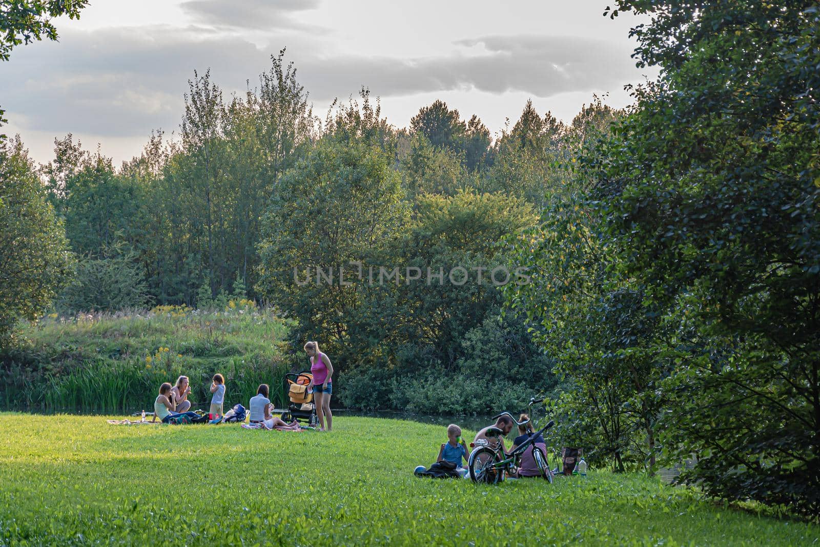 Russia, Moscow-08/20/2016: Family vacation on the green grass near the reservoir by Grommik