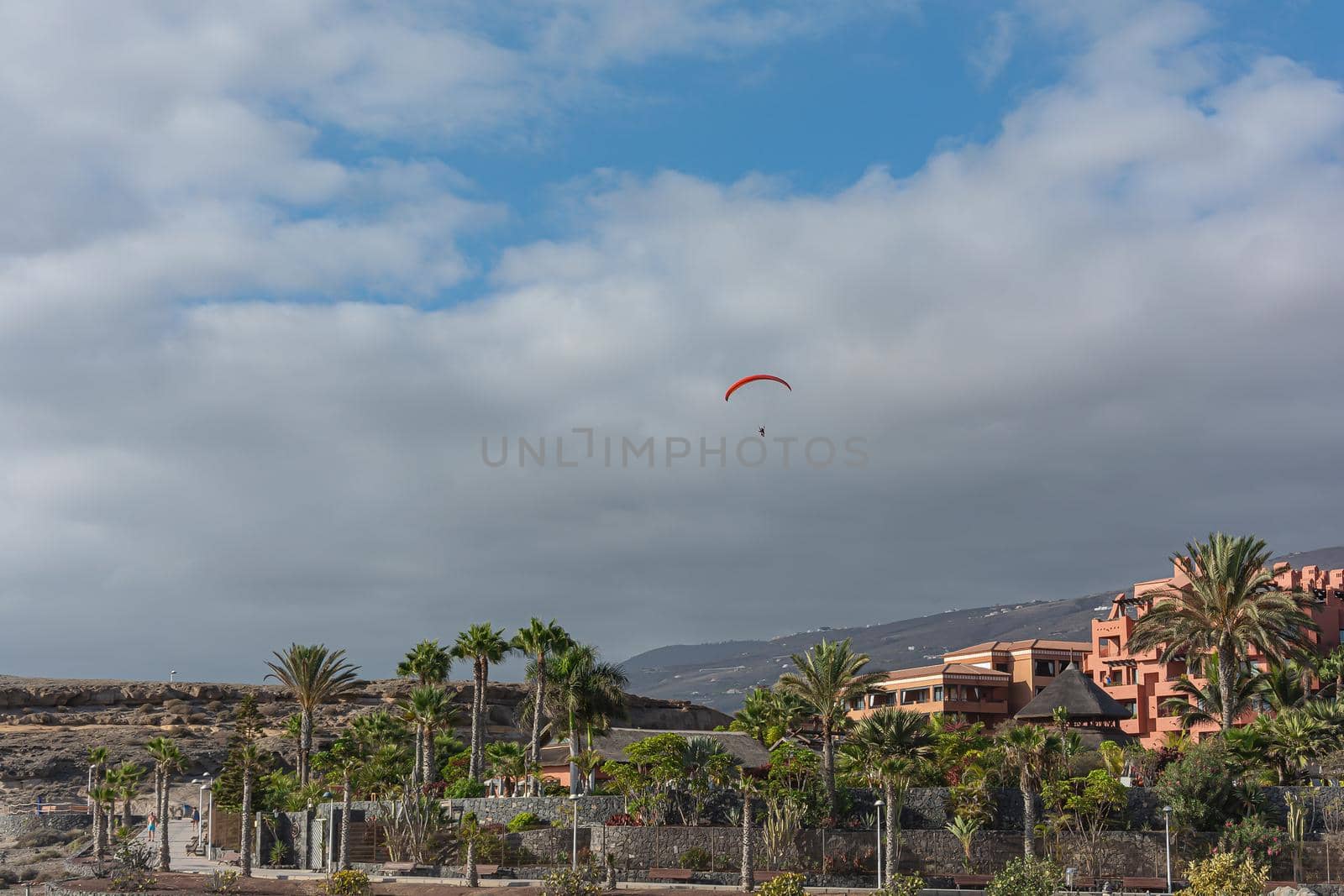 paraglider soars over mountainous terrain and buildings. Stock photo