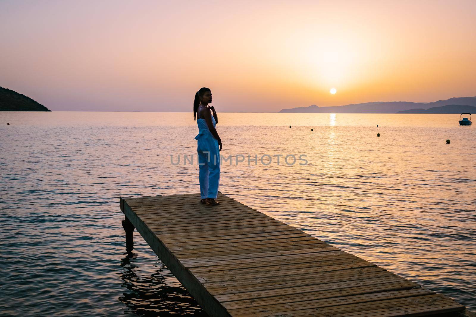 woman standing on a wooden jetty, looking at colorful sunset on the sea, men, and women watching a sunset in Crete Greece. Europe