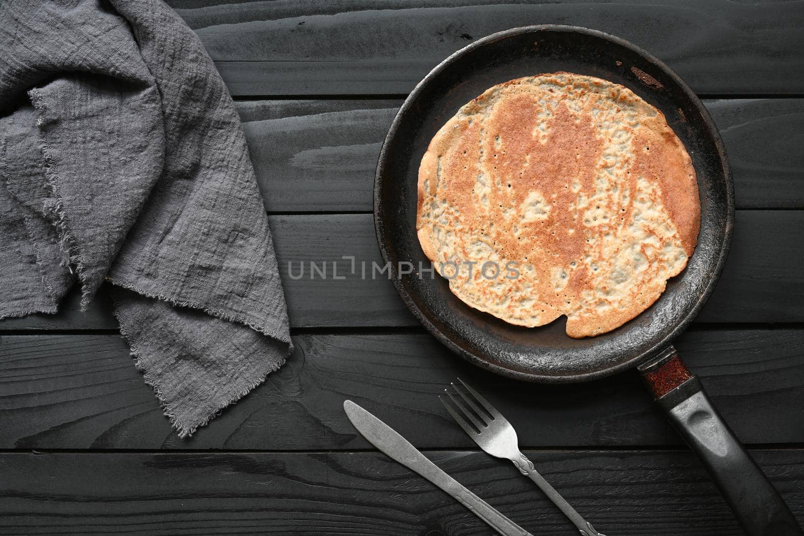 Hot pancake in black pan on black table with flour.