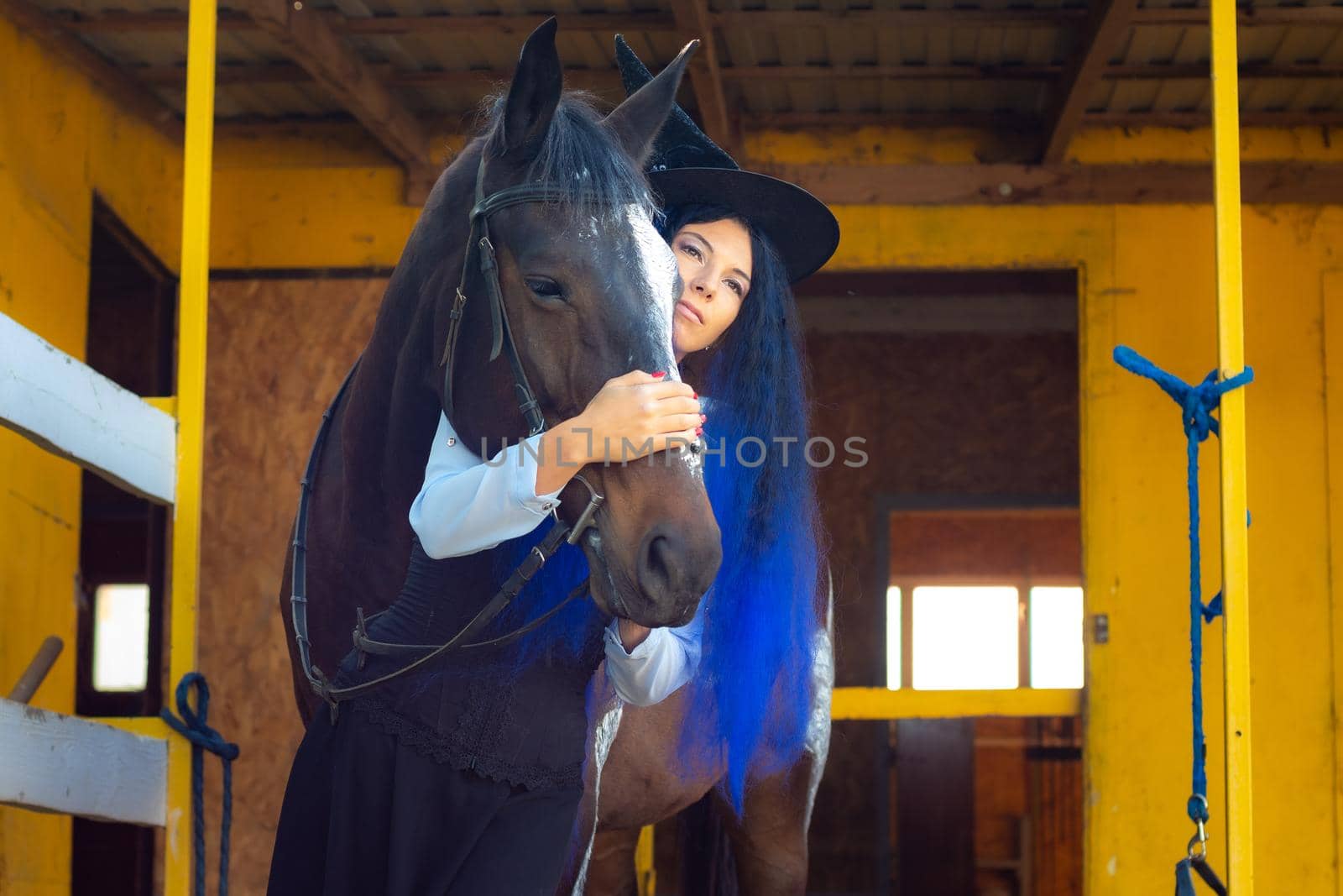 A girl dressed as a witch hugs a horse and looks thoughtfully into the distance
