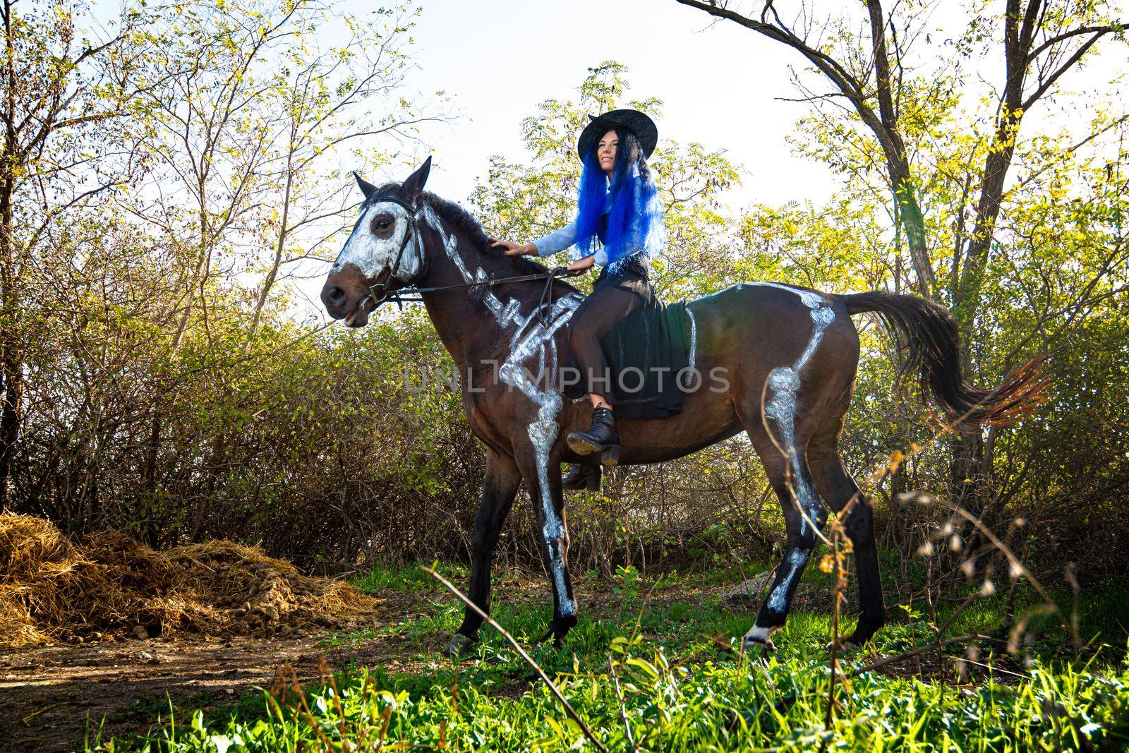 A girl dressed as a witch rides a horse on which a skeleton is painted in white paint by Madhourse