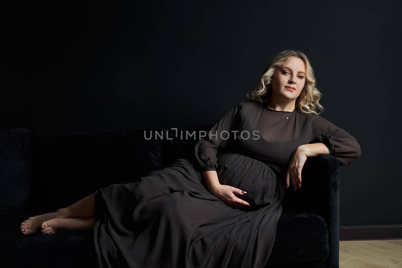 Pregnant Woman Posing In An Elegant black Dress indoors studio black wall background Blonde caucasian middle age female six month pregnancy