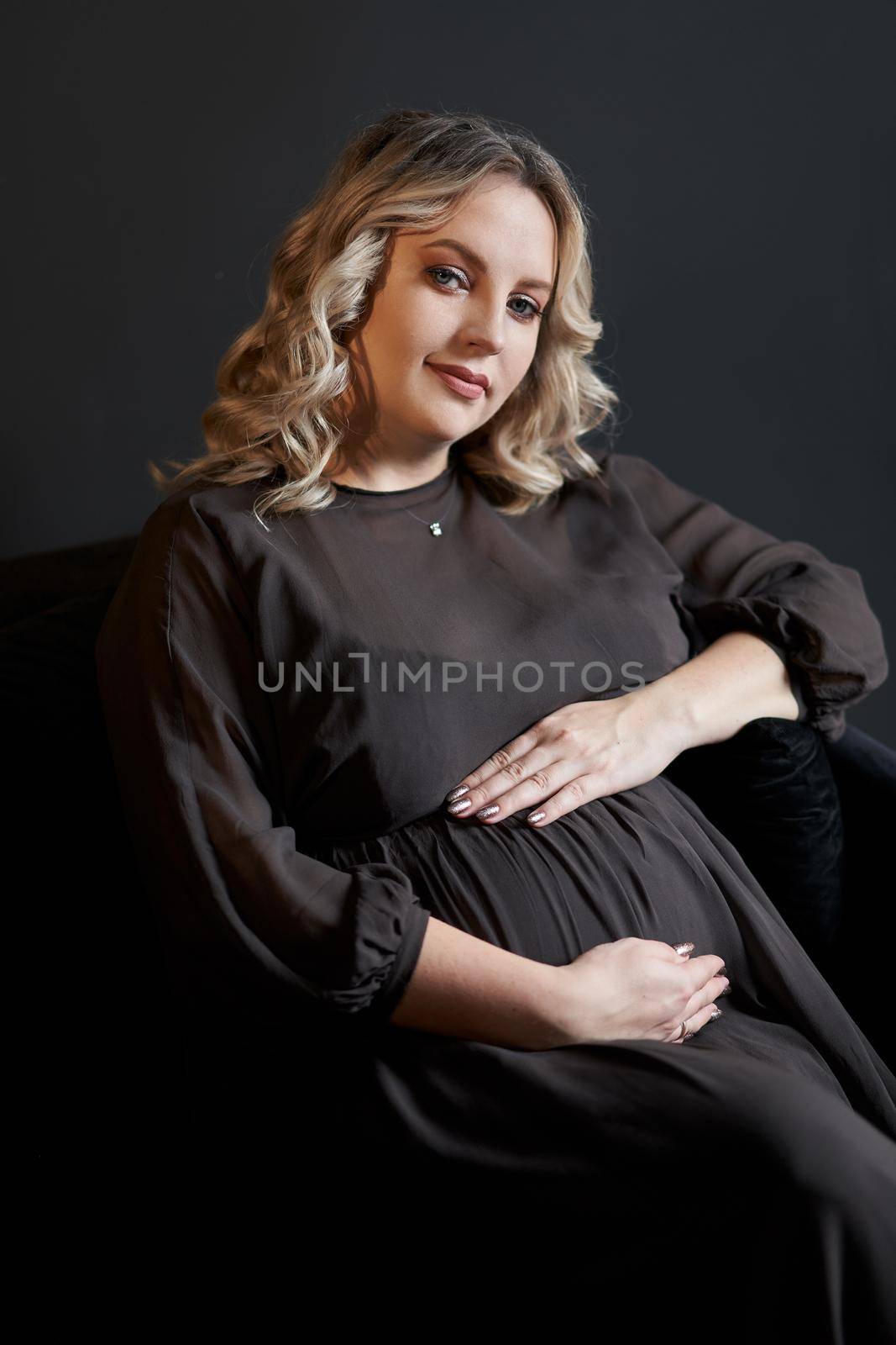 Pregnant Woman Posing In An Elegant black Dress indoors studio black wall background Blonde caucasian middle age female six month pregnancy