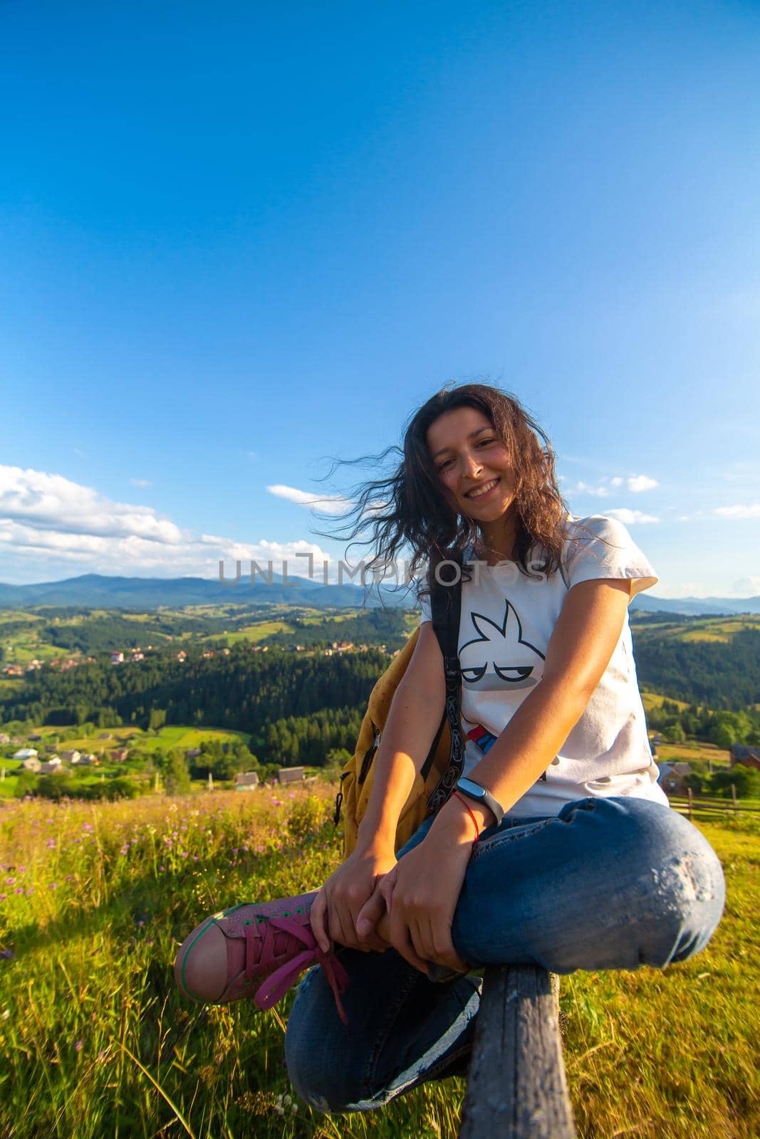 Happy gorgeous girl enjoy hills view sitting in flower field on the hill with breathtaking nature landscape.