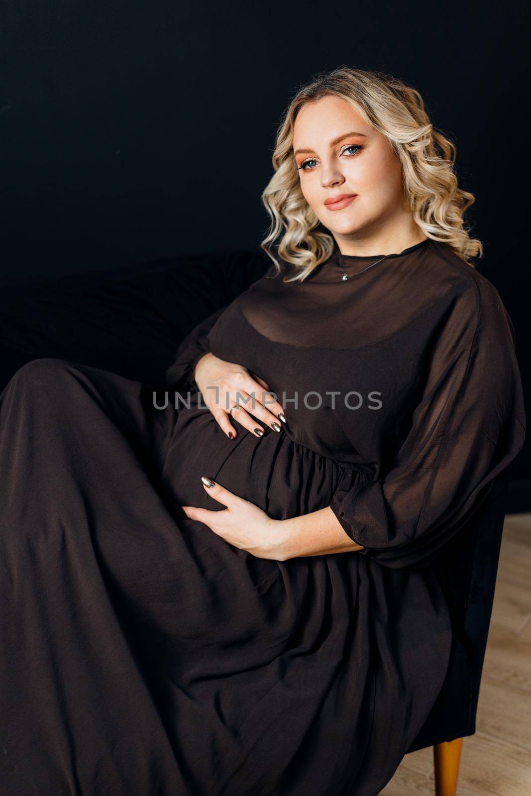 Pregnant Woman Posing In An Elegant black Dress indoors studio black wall background Blonde caucasian middle age female six month pregnancy